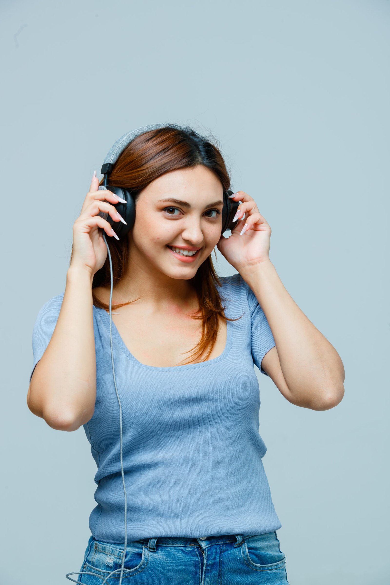 young lady holding hands on headphones while listening to music in t-shirt and looking happy. front view.